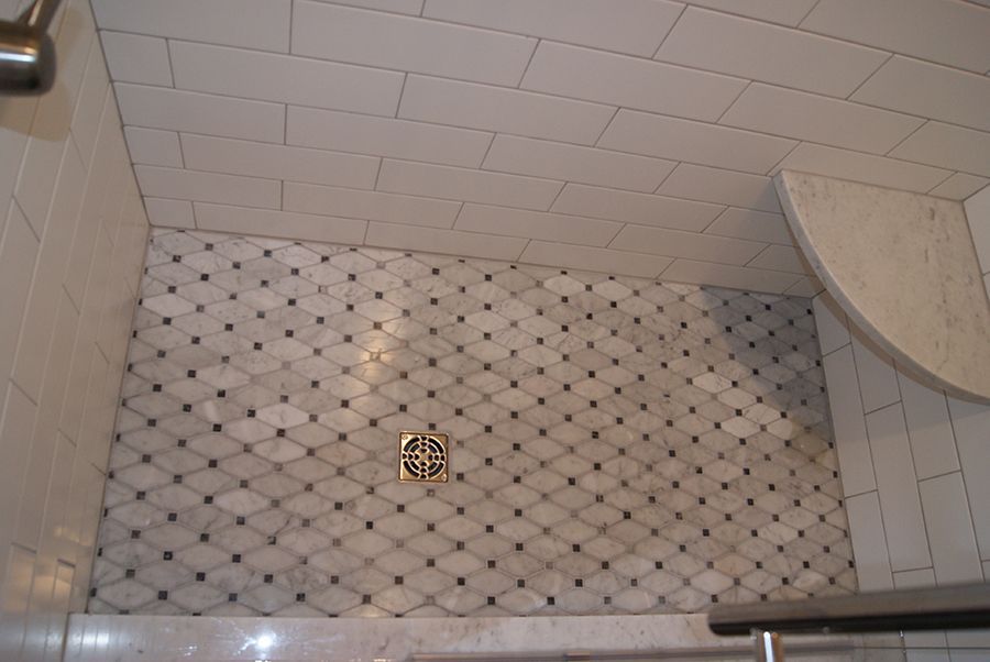 Shower with white and patterned tile, a drain, and a built-in curved shelf.