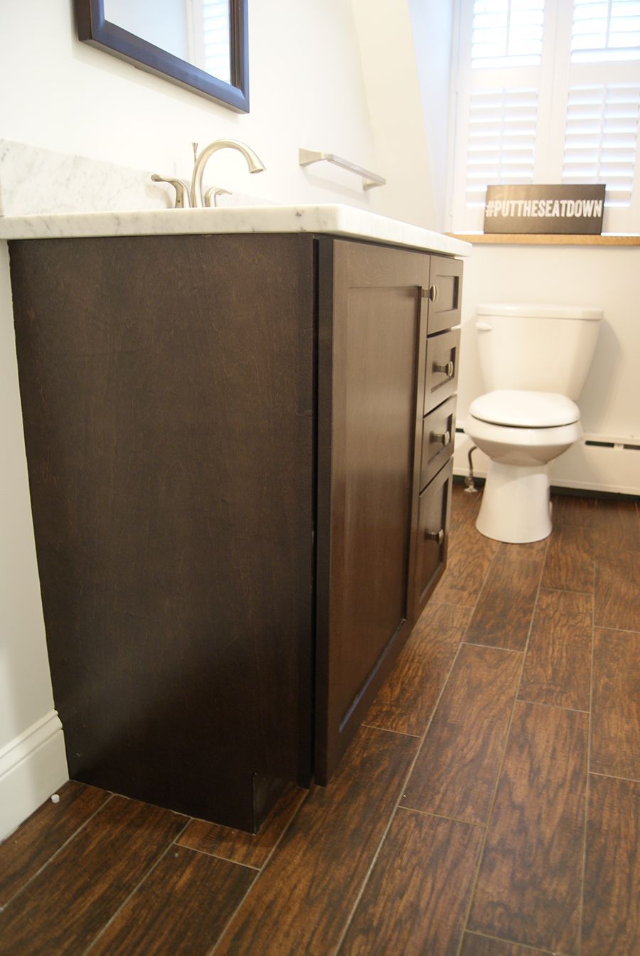 Dark wood bathroom vanity with white countertop, next to a toilet and wood-look flooring.