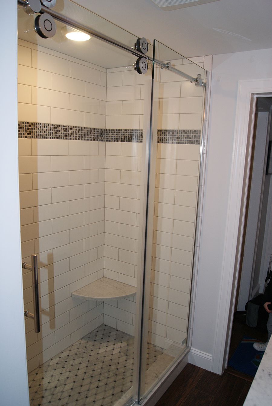 Shower with sliding glass doors, white tiled walls, corner seat, dark floor.