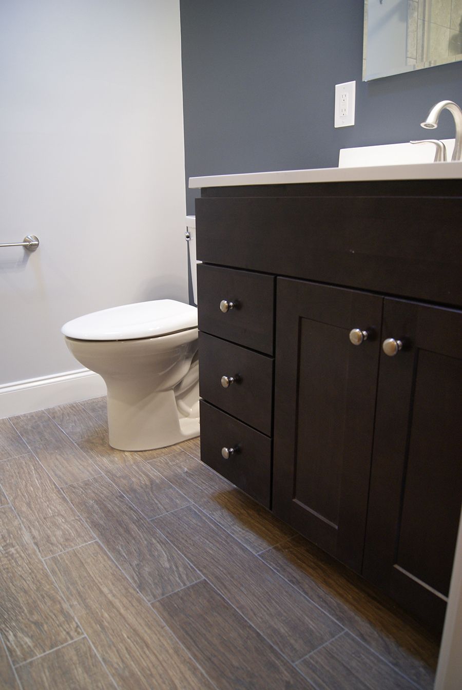 Bathroom with dark brown vanity, toilet, and gray wood-look tile flooring. Walls are blue and light gray.