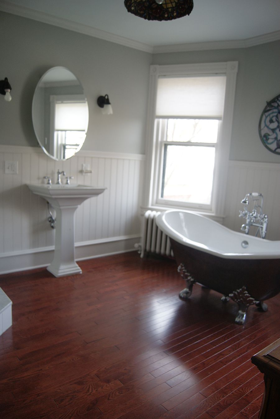 Bathroom with pedestal sink, clawfoot tub, wood floor, and window.