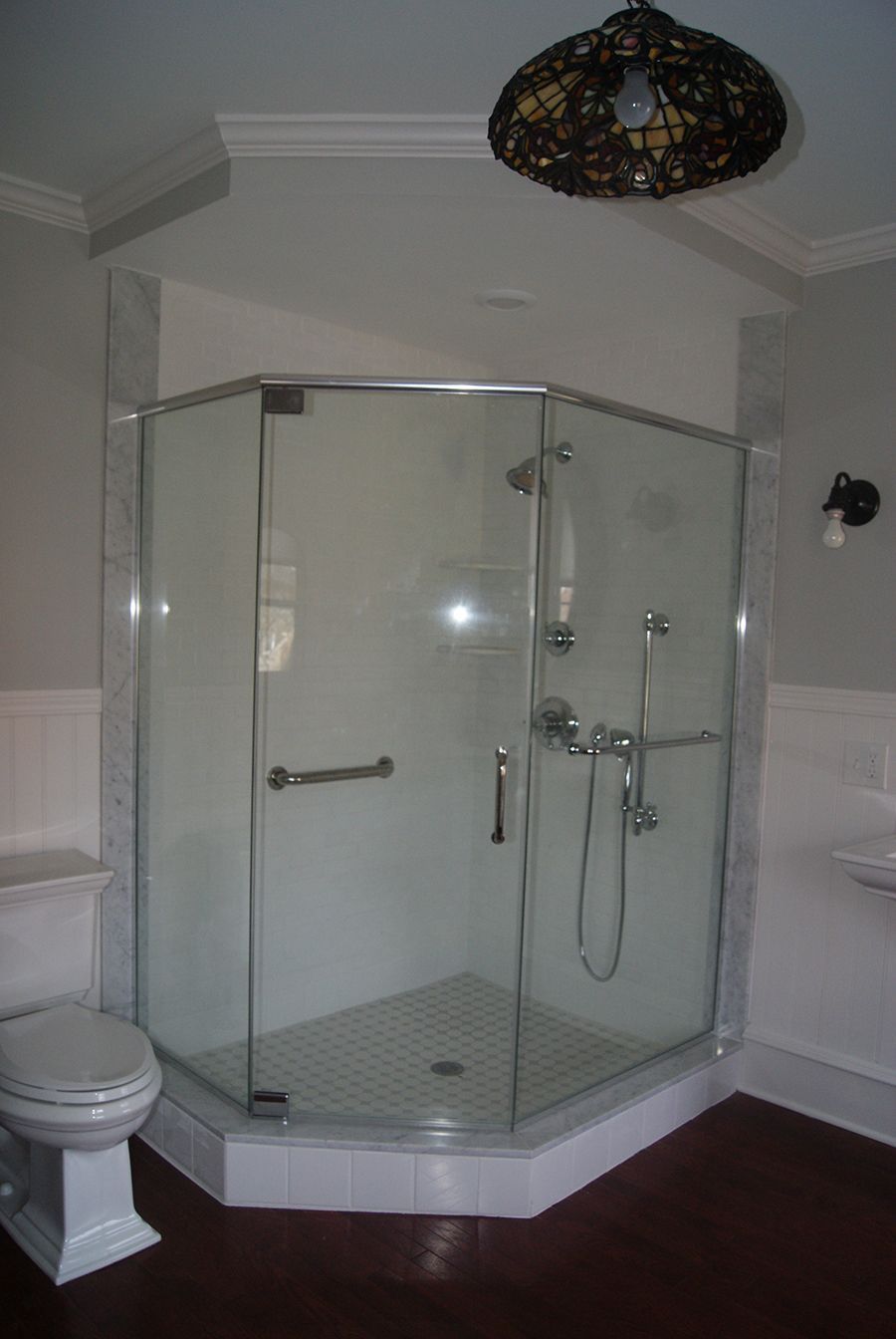 A corner glass shower in a bathroom with a toilet and a dark floor.