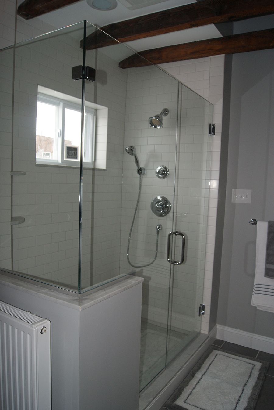 Glass shower enclosure with gray tiled walls, silver fixtures, and exposed wooden beams.