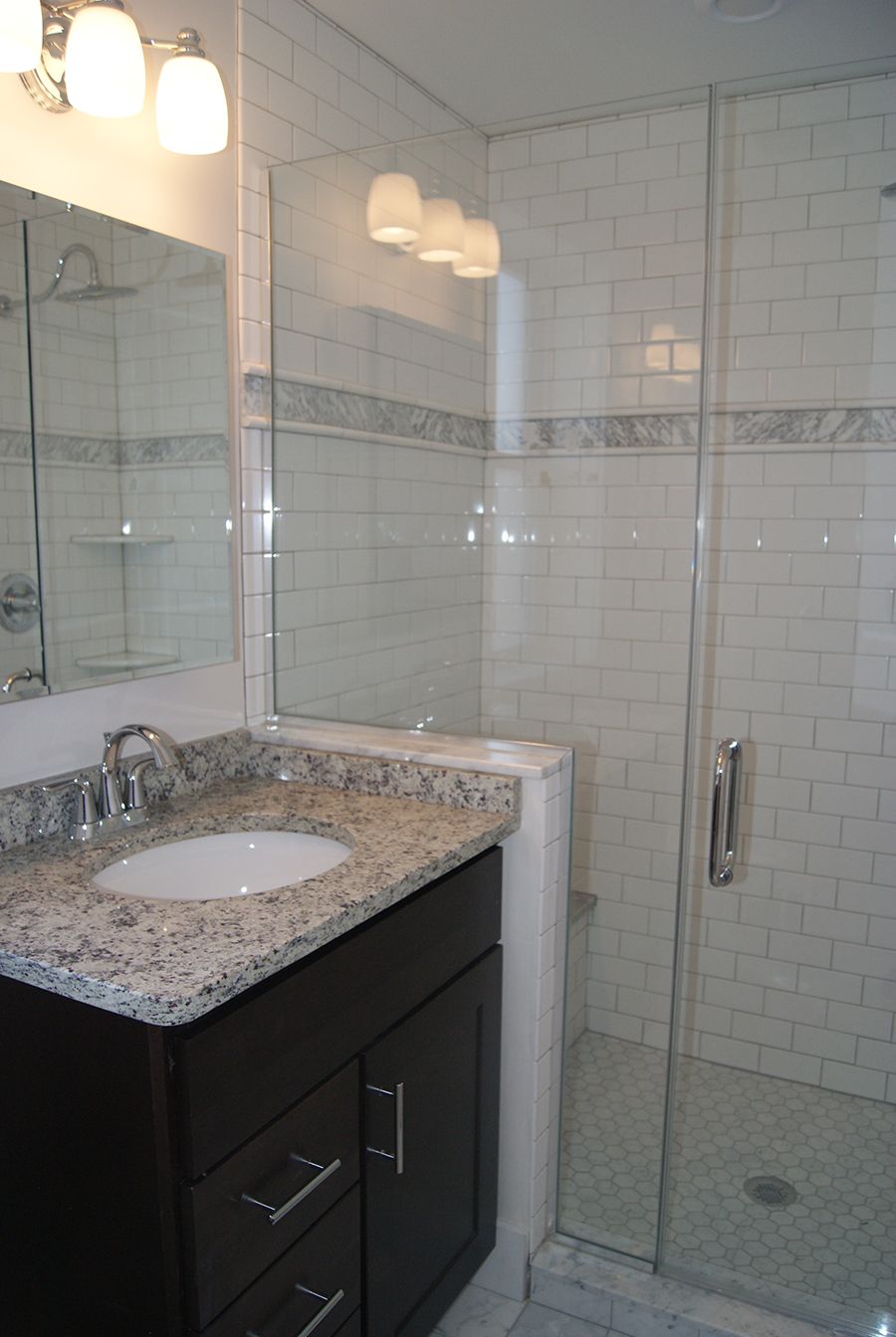 Bathroom with a dark vanity, granite countertop, white tile walls, and a glass shower enclosure.