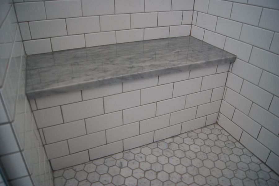 White tiled shower with a gray marble bench and a hexagon tile floor.