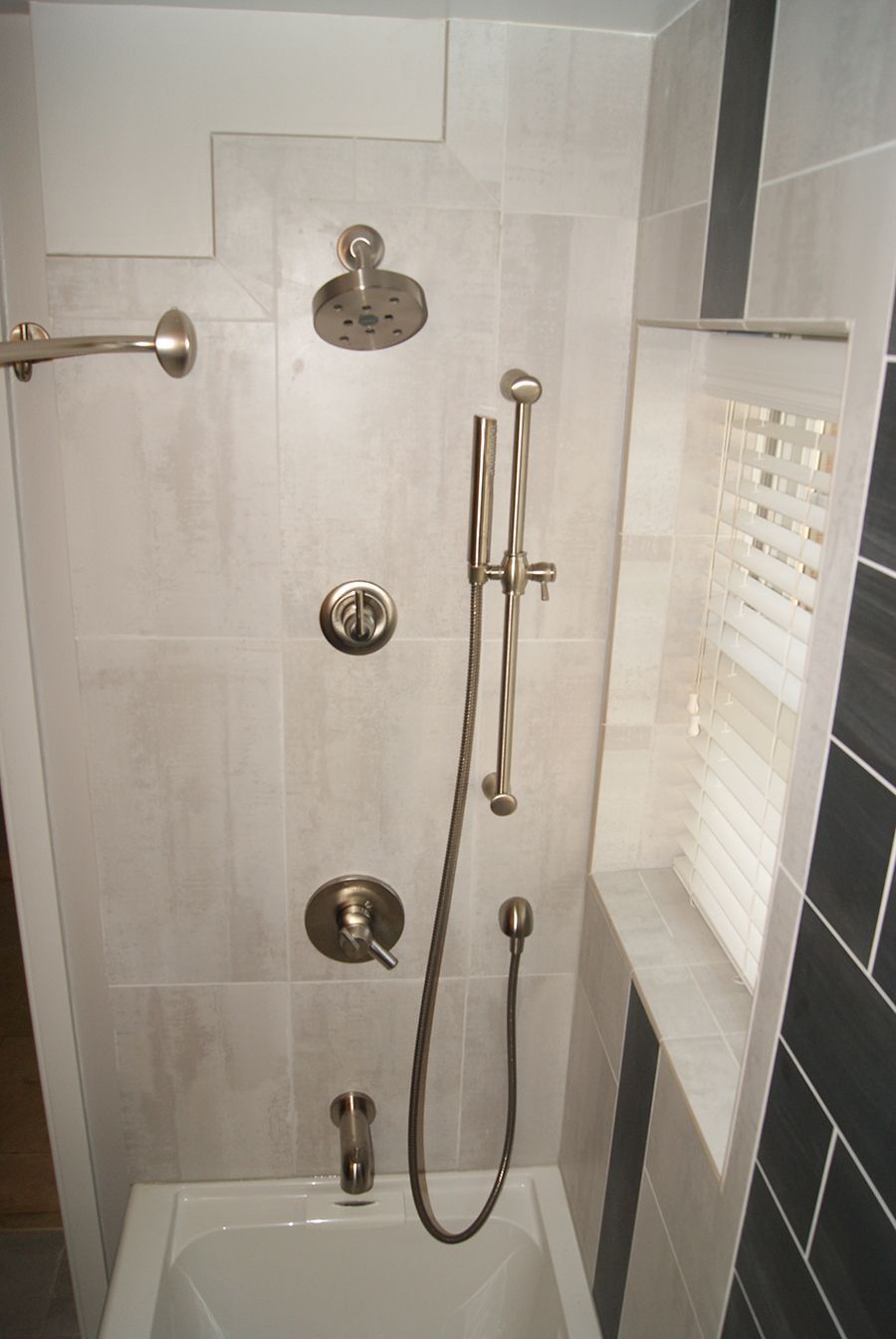 Shower stall with light gray tiled walls and multiple chrome shower fixtures.