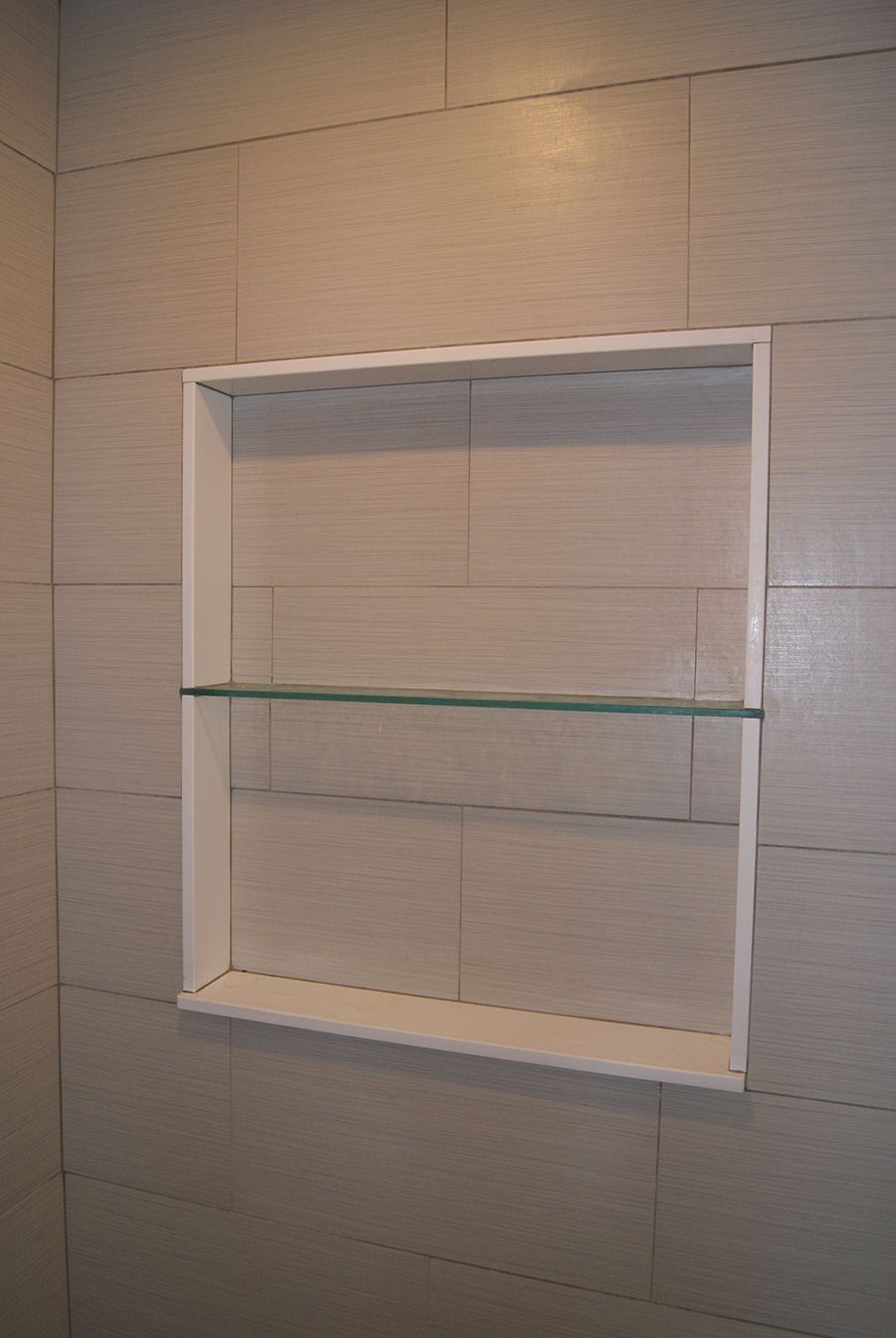 Recessed shower niche with a glass shelf, surrounded by tiled walls.