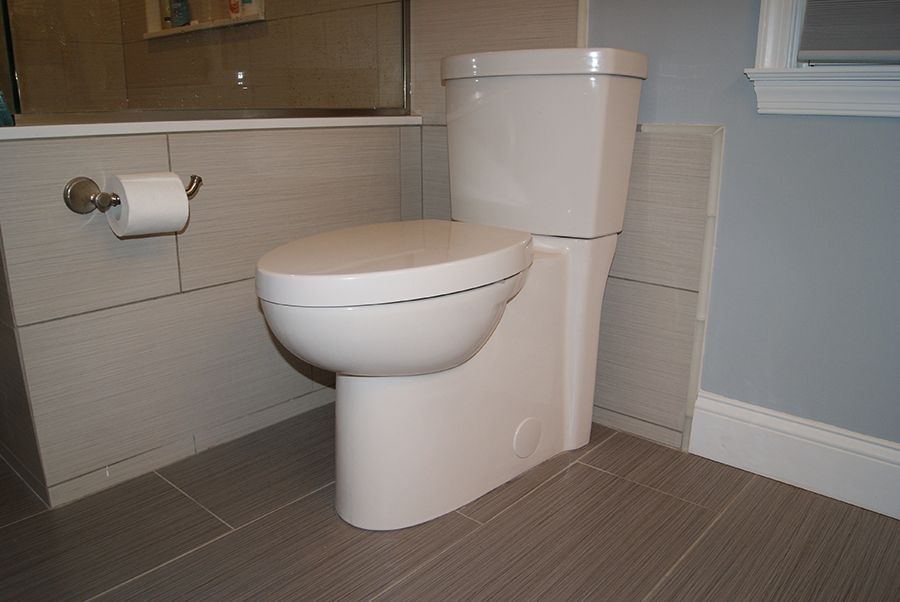 White toilet in a bathroom with gray tile floor and walls; toilet paper roll mounted on wall.
