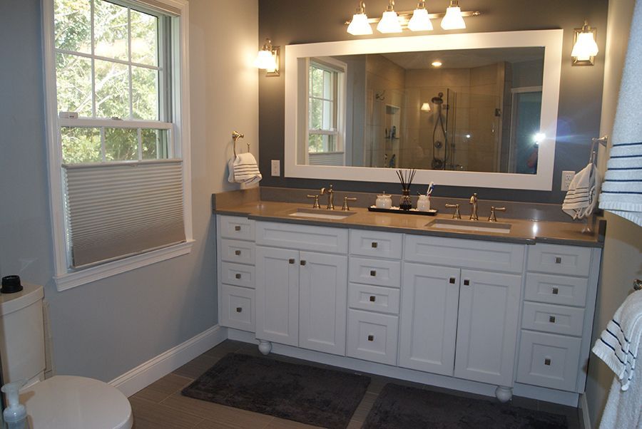 Bathroom with white double vanity, large mirror, window, gray walls, and dark gray rug.