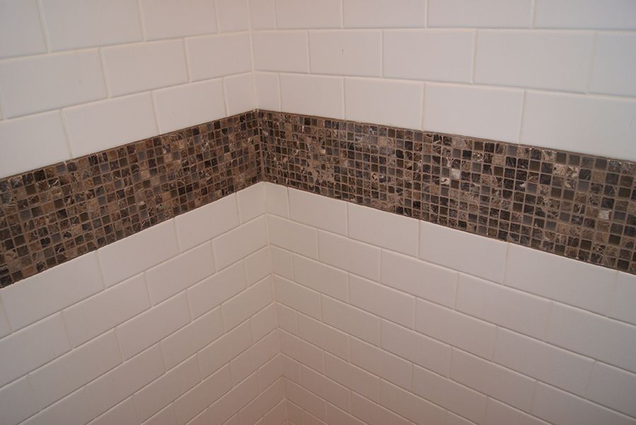 White tiled bathroom corner with a brown mosaic tile border.