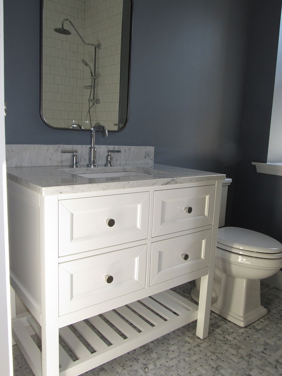 White bathroom vanity and toilet, marble countertop, silver faucet, blue wall, mirror.