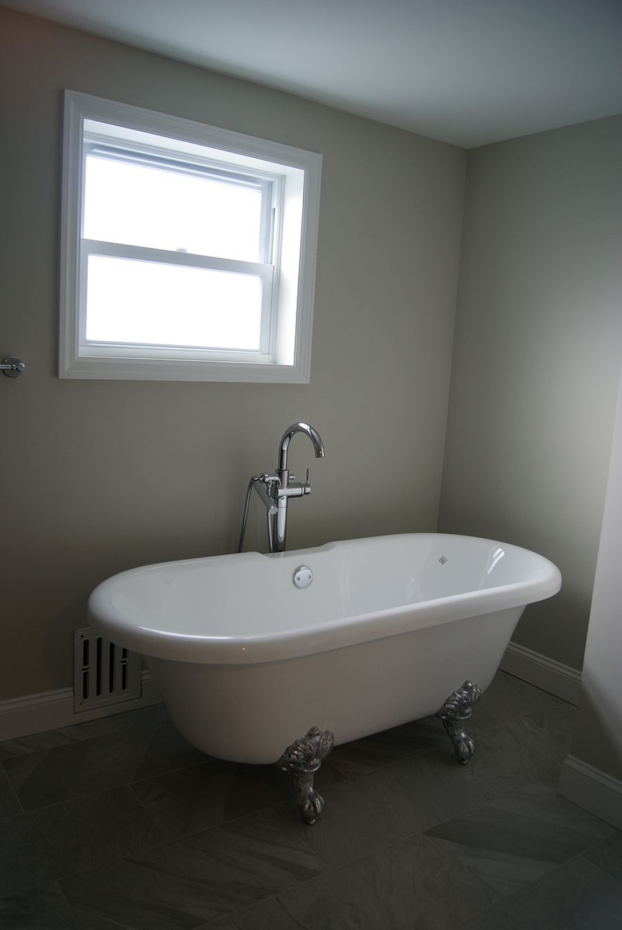 White clawfoot tub in a bathroom with a window, chrome faucet, and gray walls.