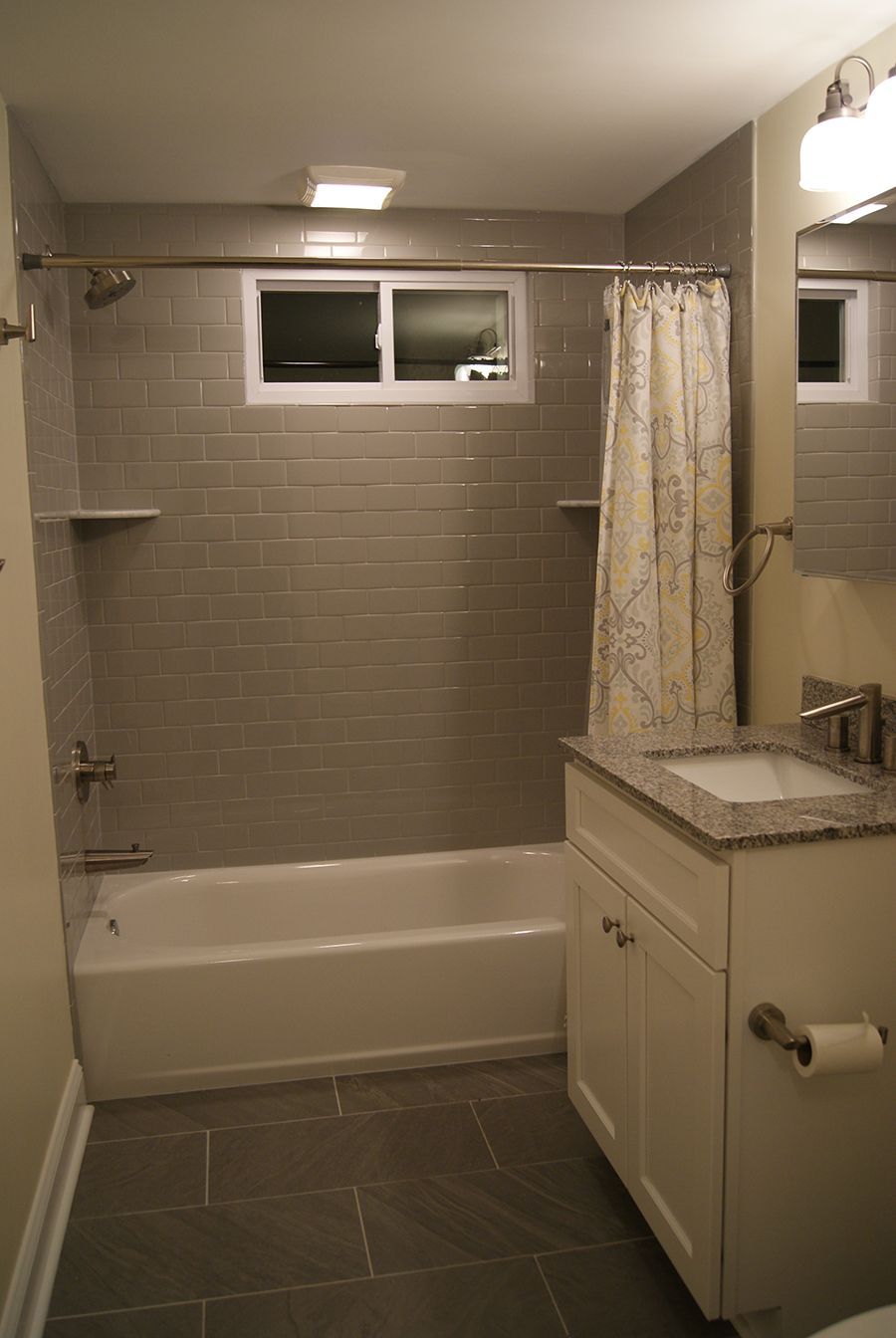 Modern bathroom with gray tile, white tub, vanity, window, shower curtain, and a gray floor.