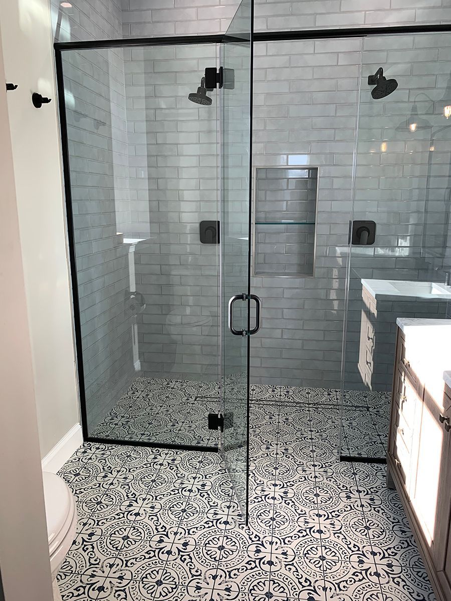 Modern shower stall with glass doors, black trim, and patterned tile floor.