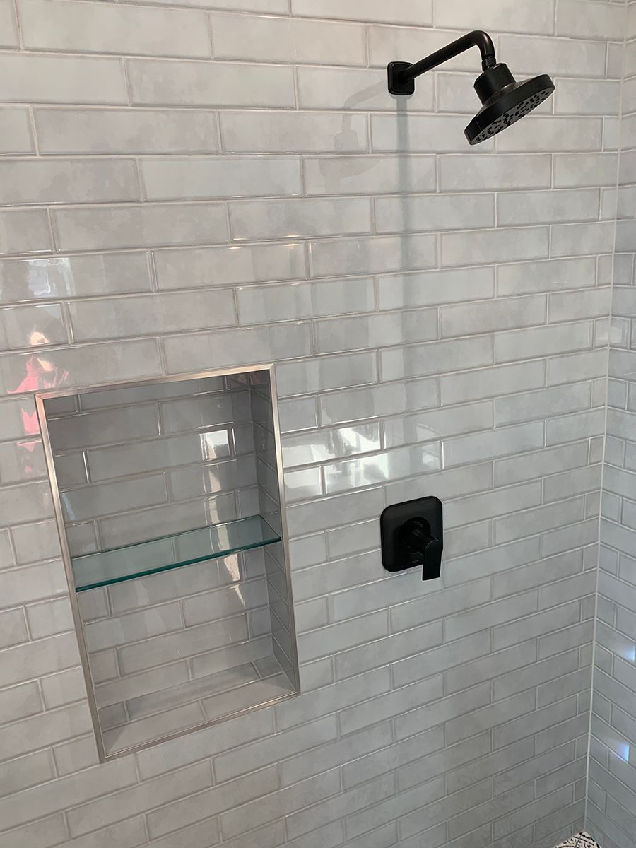 White tiled shower with black showerhead, control, and recessed shelf.
