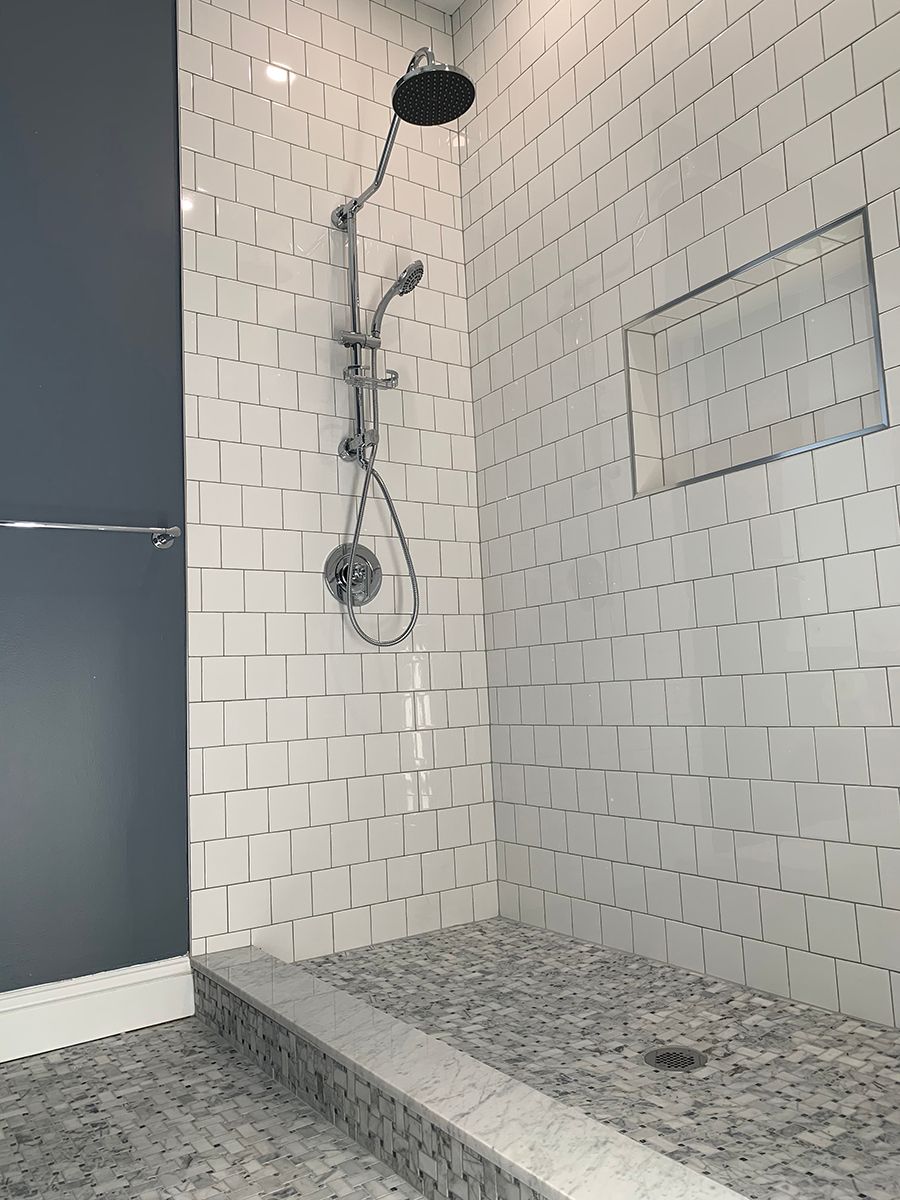Shower with white, textured tile walls and grey stone floor. Chrome shower fixtures. Blue wall on left.