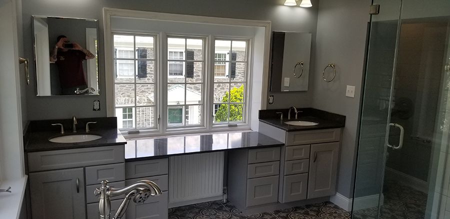 Bathroom with gray cabinets, black countertops, and a large window. A shower is visible.