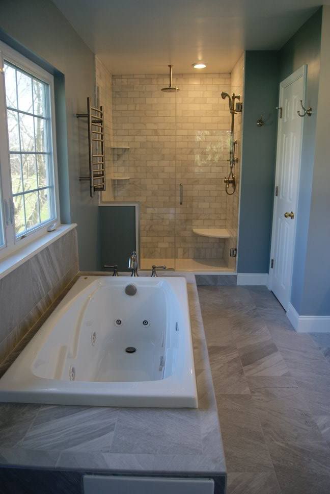 Spacious modern bathroom with a white soaking tub, glass shower, and gray tile flooring.