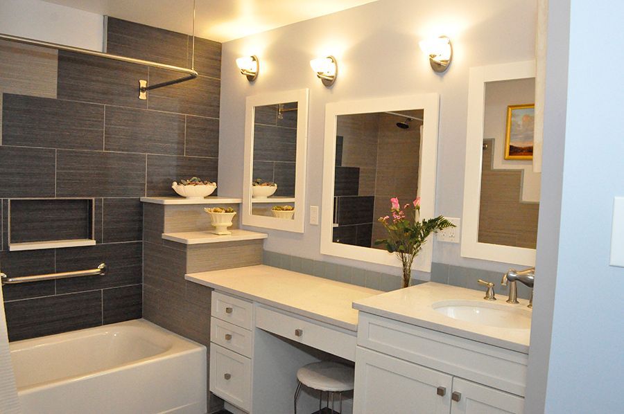 Bathroom with white vanity, gray walls, mirrors, tub, and decorative lighting.