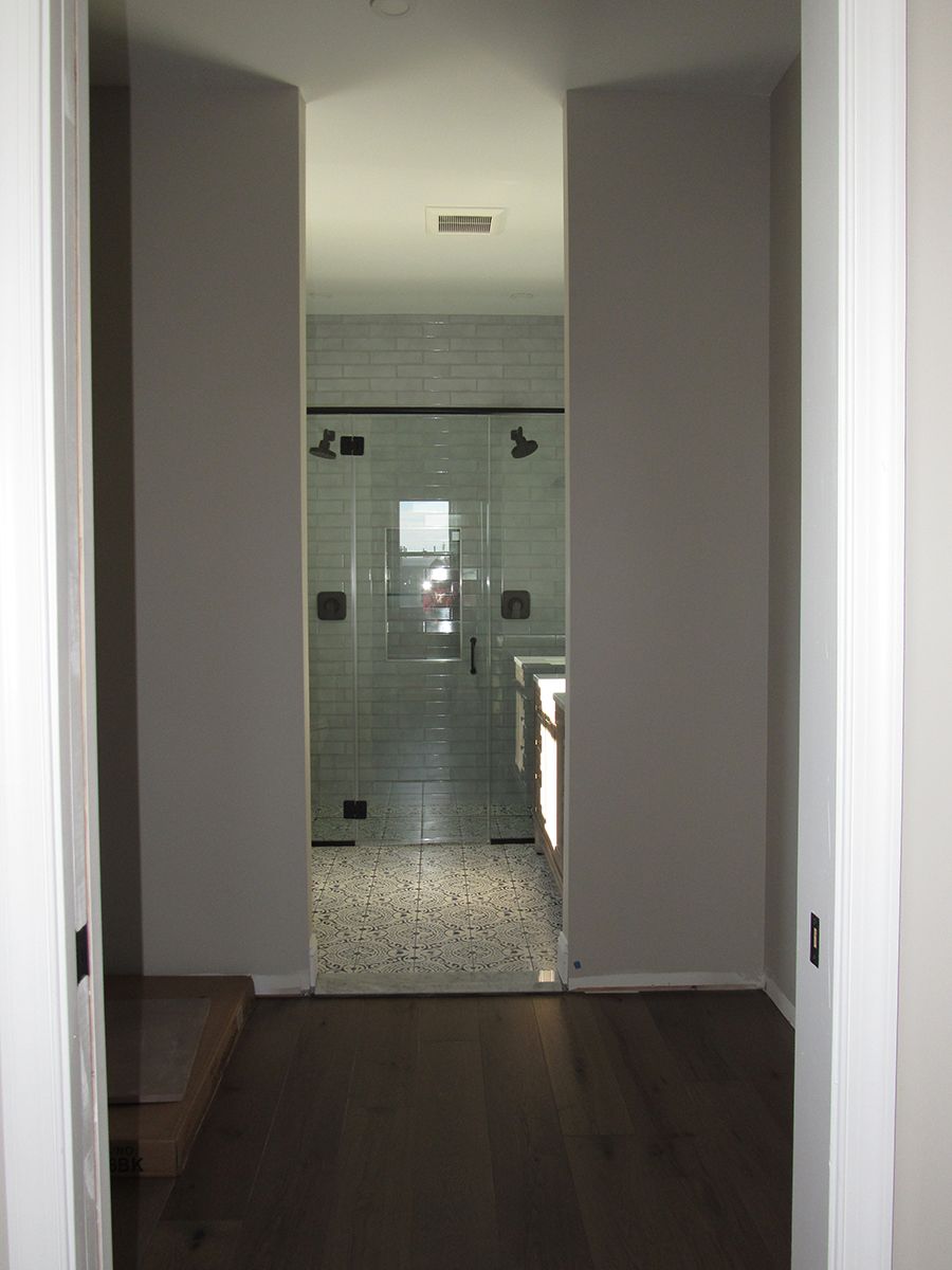 View into a bathroom. Dark wood floor, light gray walls, glass shower, and mosaic tile floor.