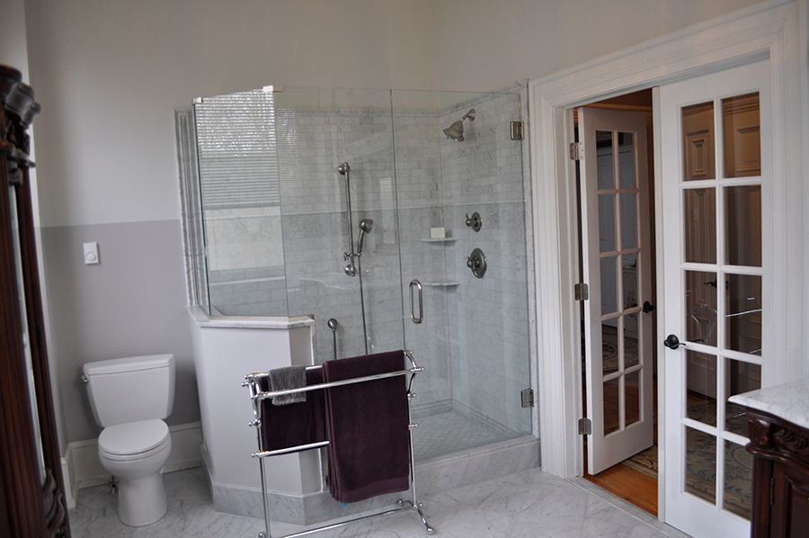 Bathroom with glass shower, toilet, and towel rack. French doors lead to another room.