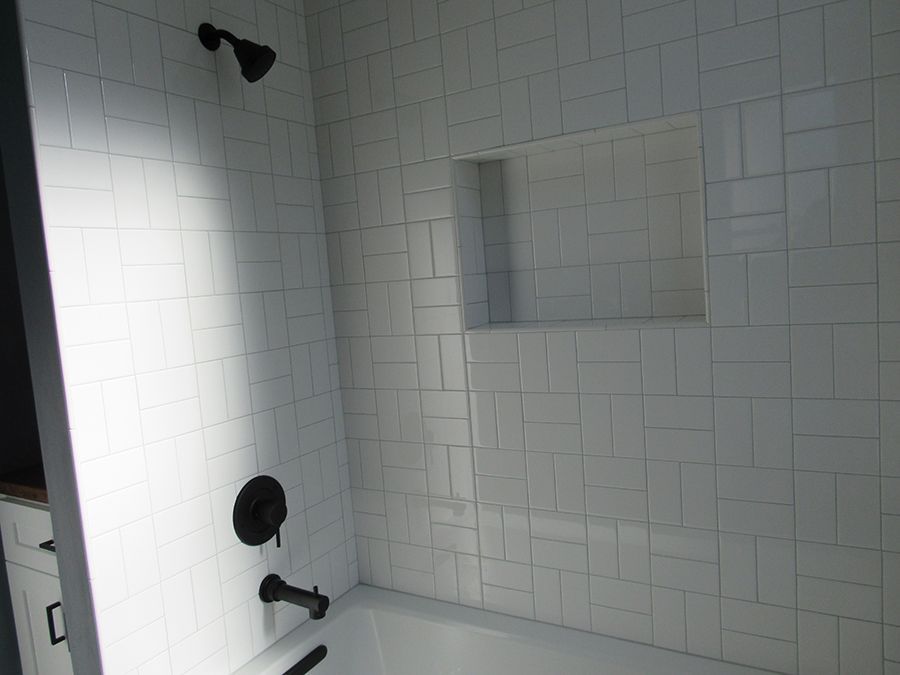 White tiled shower with a built-in shelf, black shower fixtures, and a black showerhead.