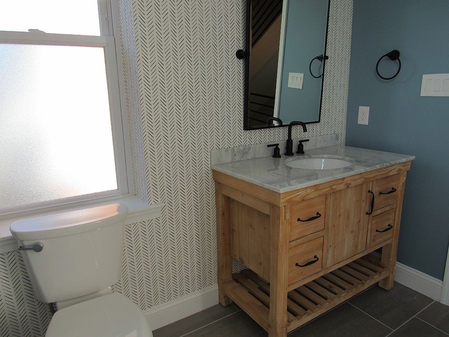 Bathroom with light wood vanity, white sink, blue wall, patterned wallpaper, and toilet.