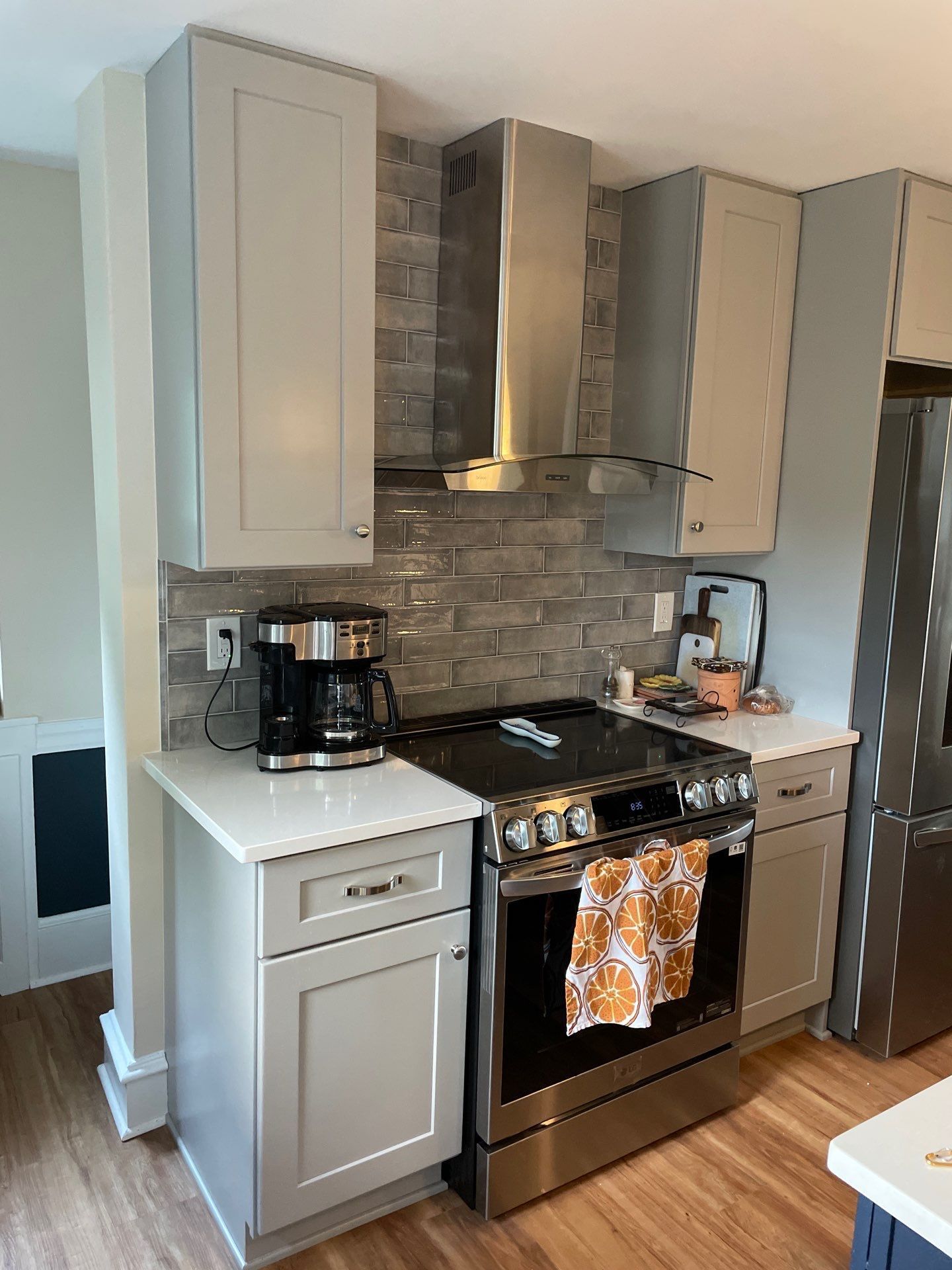 Gray and white kitchen with stove, stainless steel vent hood, cabinets, and a coffee maker.