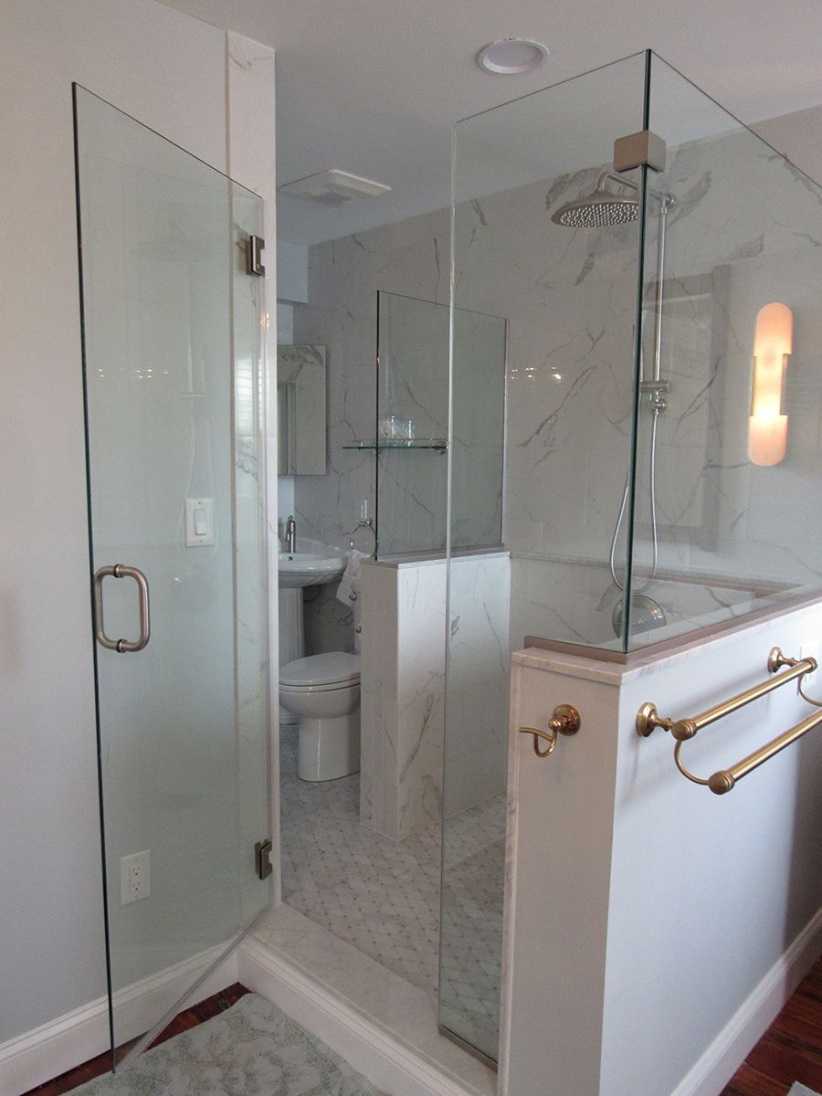 Glass-enclosed shower with a partially open door. White marble tiles, gold fixtures. Bathroom setting.