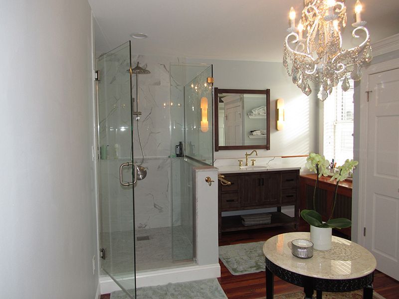 Elegant bathroom with glass shower, chandelier, dark wood vanity, and round table.