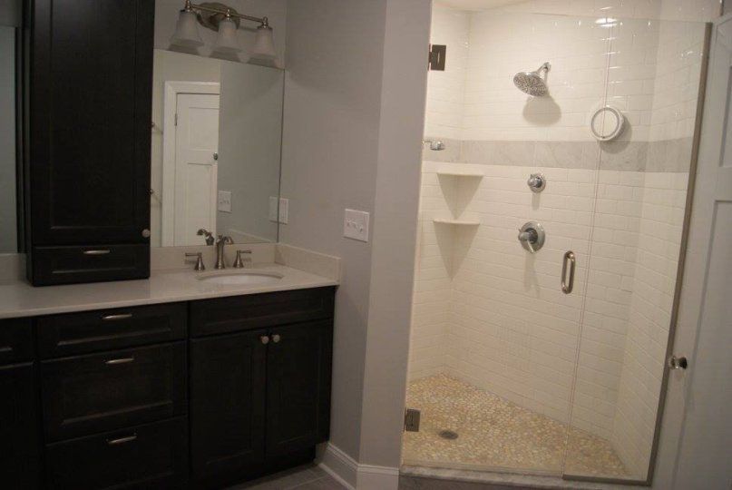 Bathroom with dark cabinets, a white countertop, a shower with pebble floor, and a large mirror.