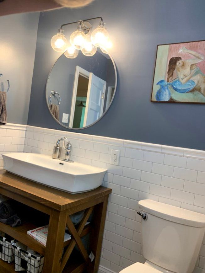 Bathroom with white subway tile, blue walls, a round mirror, and a wood vanity.