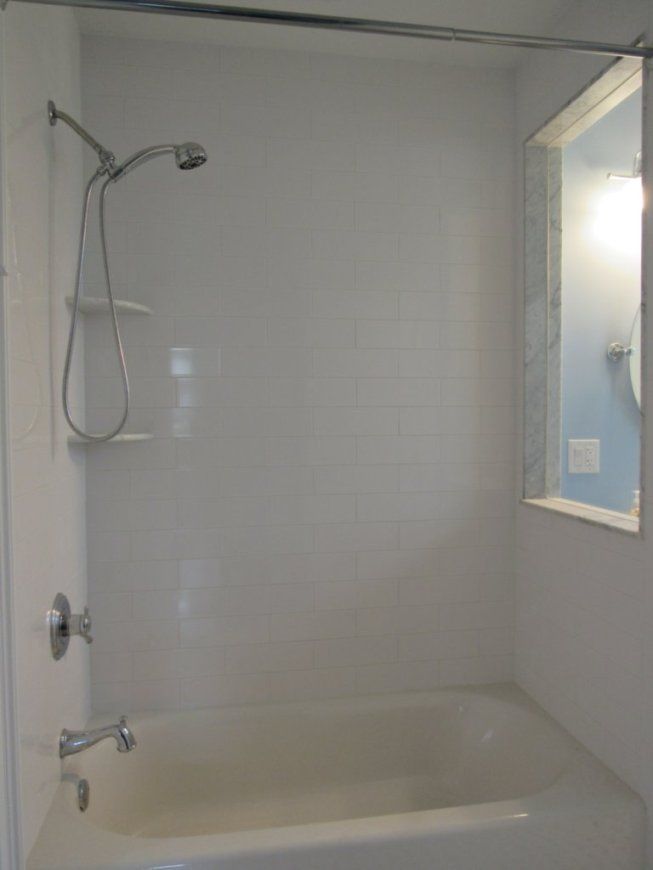 White bathtub and shower surround with handheld showerhead and open window to a light blue wall.
