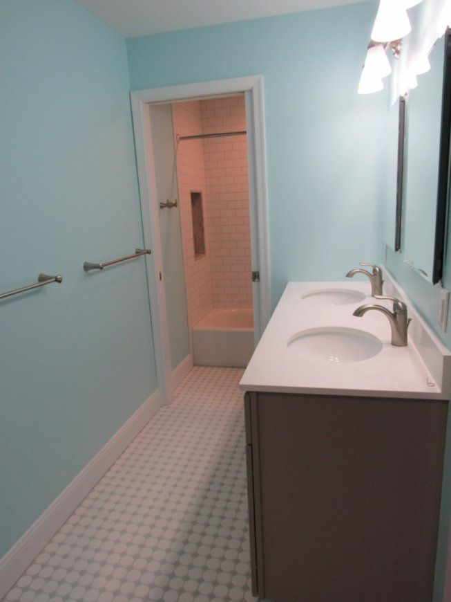 Bathroom with light blue walls, white sink with gray cabinet, and doorway to a shower.