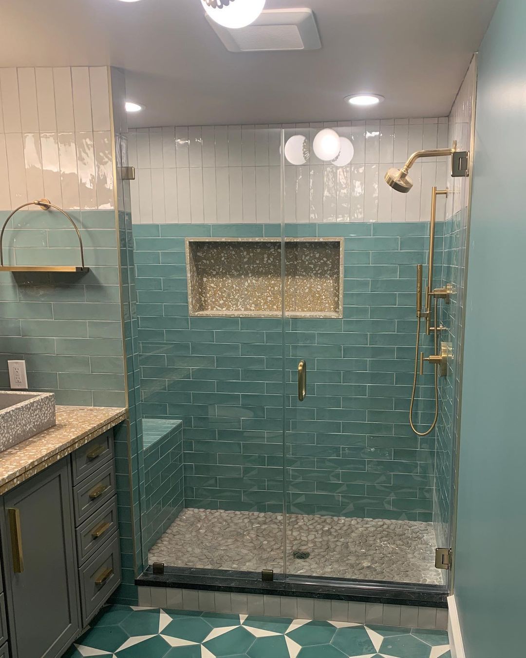 Teal-tiled shower with a clear glass door, gold fixtures, and a pebble floor.