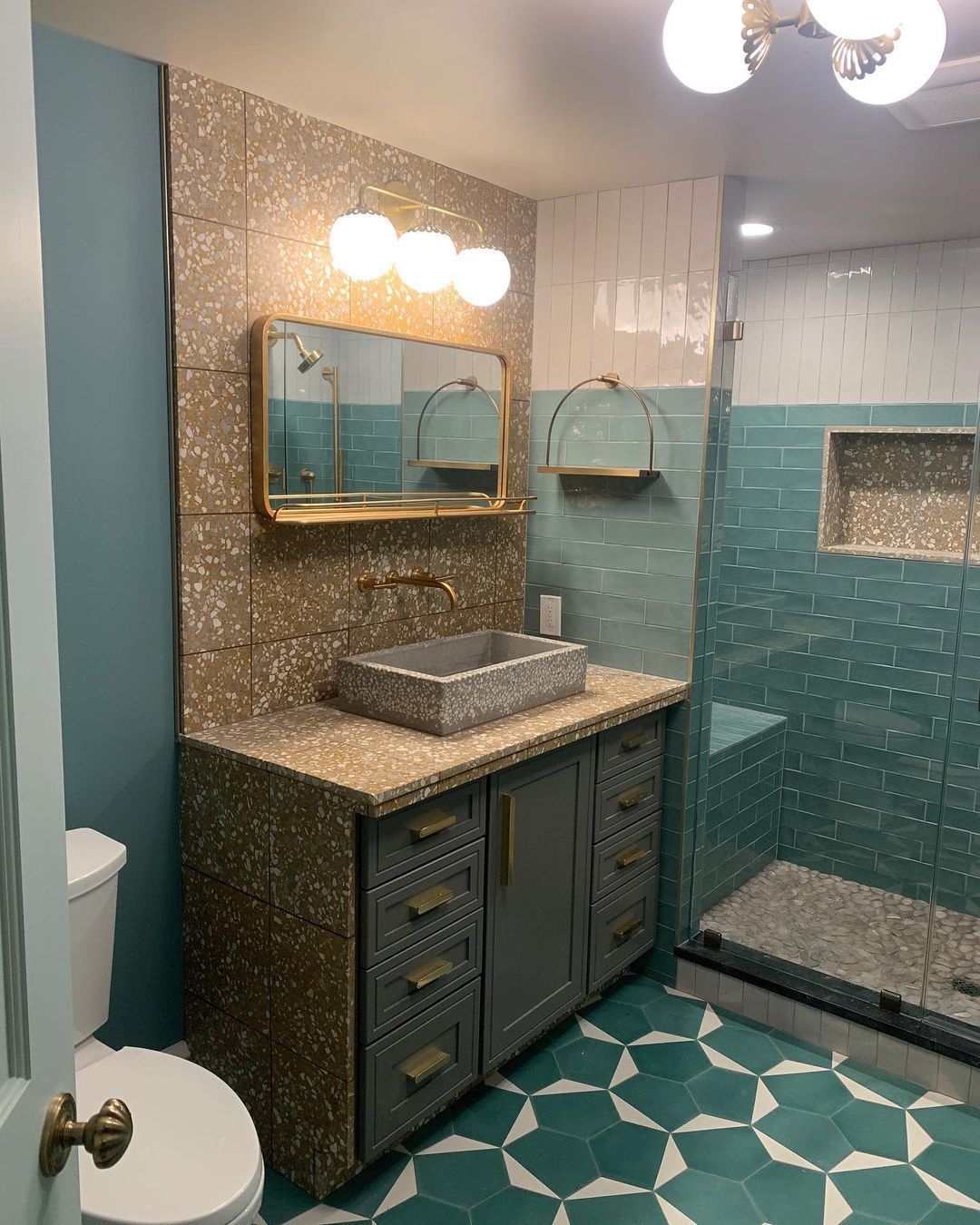 Bathroom with blue and terrazzo walls, gray vanity, and teal tile floor.