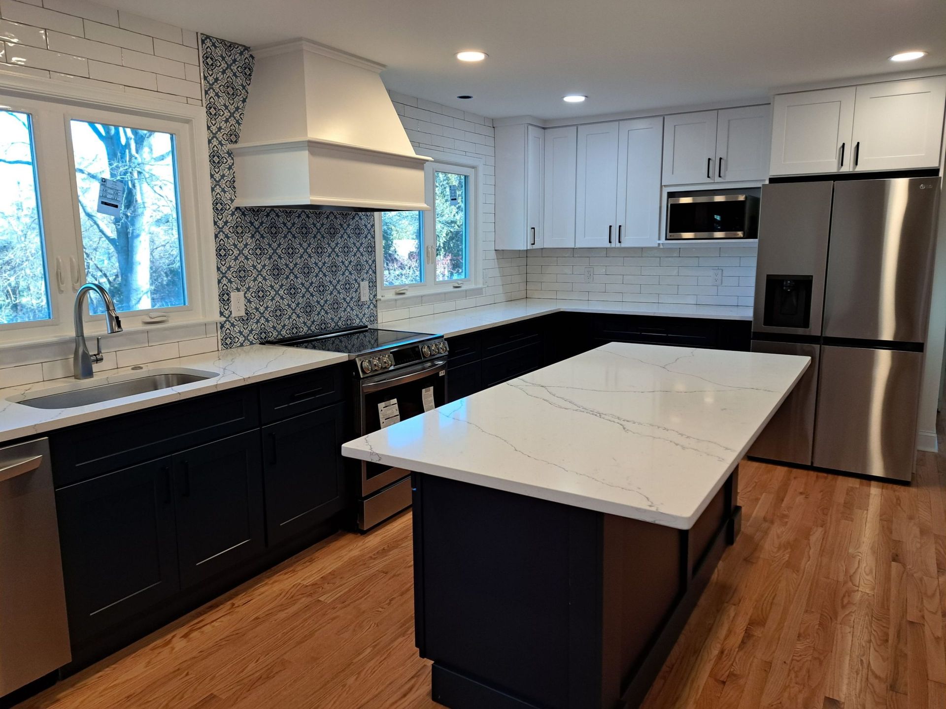Modern kitchen with white and navy cabinets, stainless steel appliances, and a marble island.