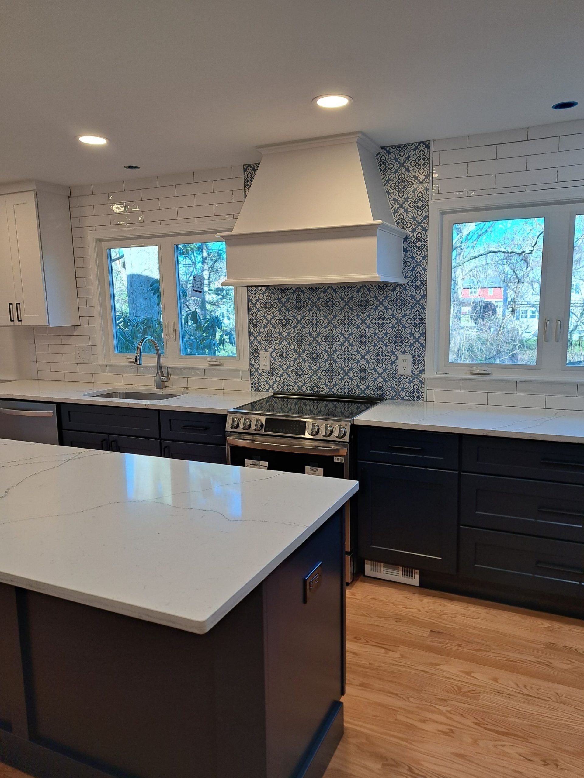 Modern kitchen with navy cabinets, white countertops, stainless steel appliances, and mosaic tile backsplash.