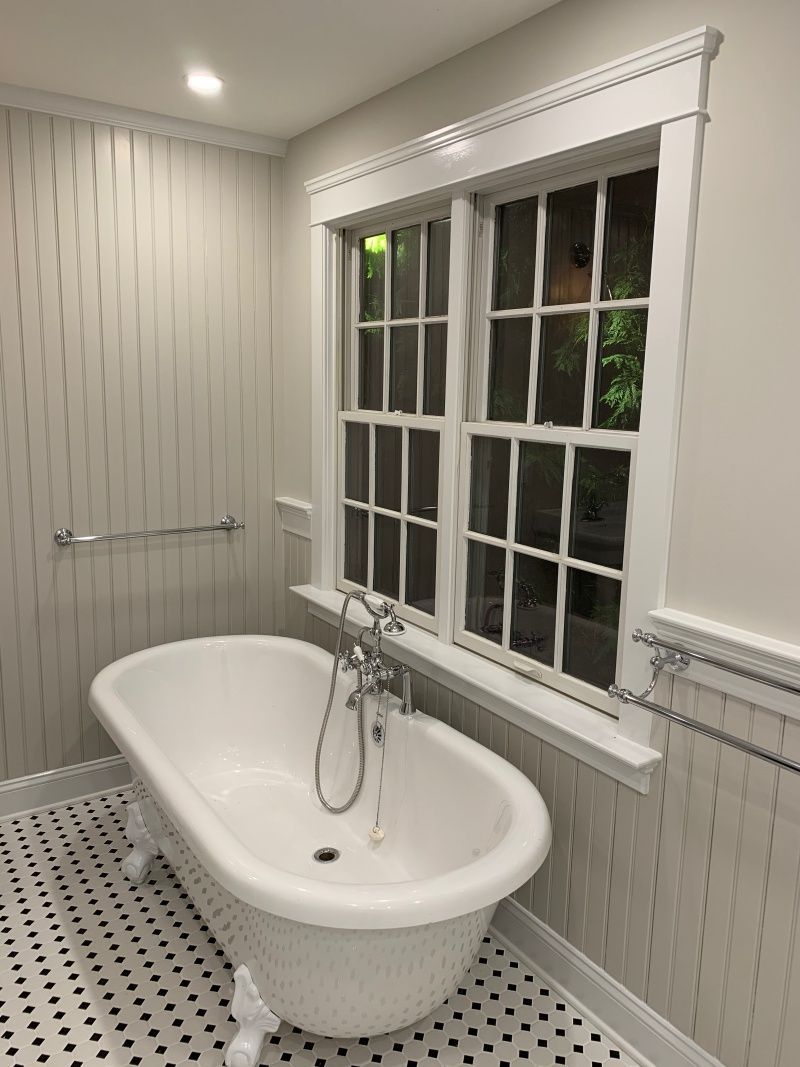 Bathroom with clawfoot tub, window, and black and white tiled floor.