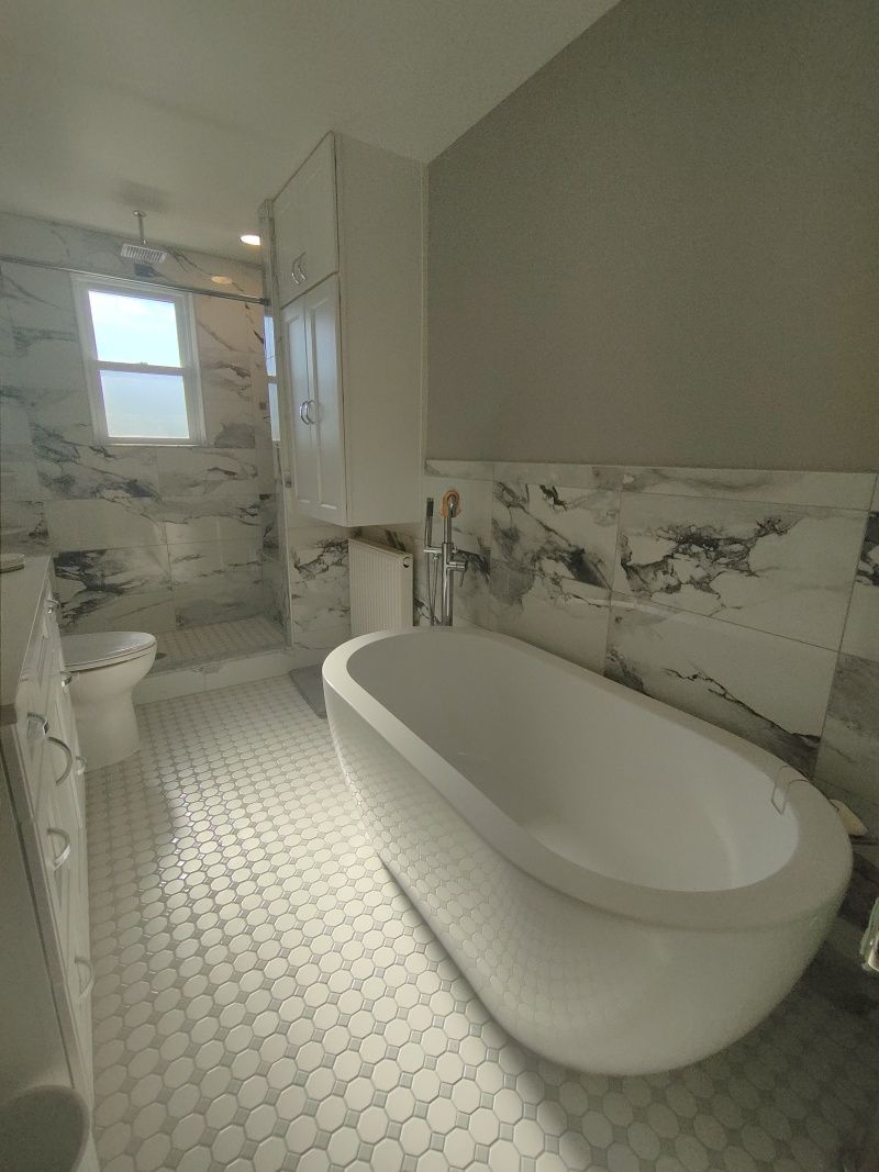 White bathroom with a freestanding tub, toilet, and marble tile walls and floor.