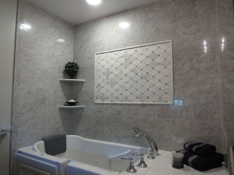 Bathroom with a white jacuzzi tub, gray tiled walls, decorative shelves, and a patterned wall insert.