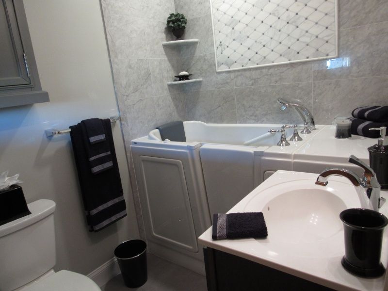 Bathroom with a walk-in tub, sink, and toilet. Gray and white color scheme, black towels and accessories.