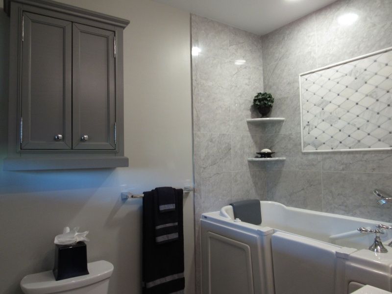 Bathroom interior with a gray cabinet, toilet, tub, and tiled walls.