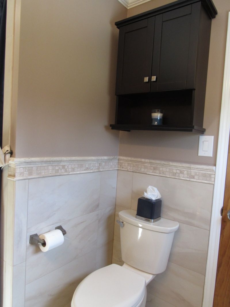 Bathroom with toilet, wall-mounted cabinet, and decorative tile. Beige and dark brown tones.