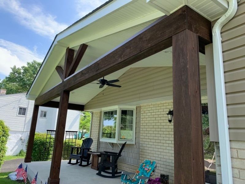 A covered porch with dark brown beams and columns. Rocking chairs sit in front of a window.