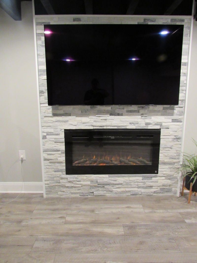 A fireplace and TV mounted on a gray and white stone wall, with gray flooring.