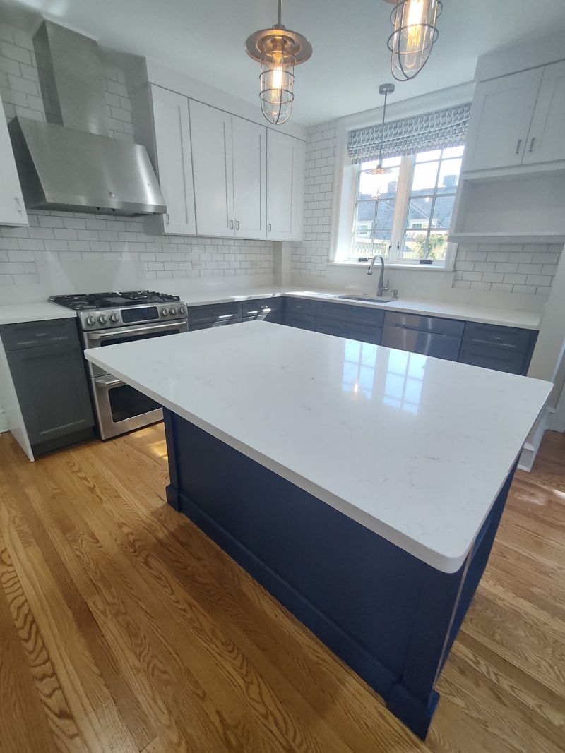 Modern kitchen with white countertops and blue island, stainless steel appliances, and wooden floors.