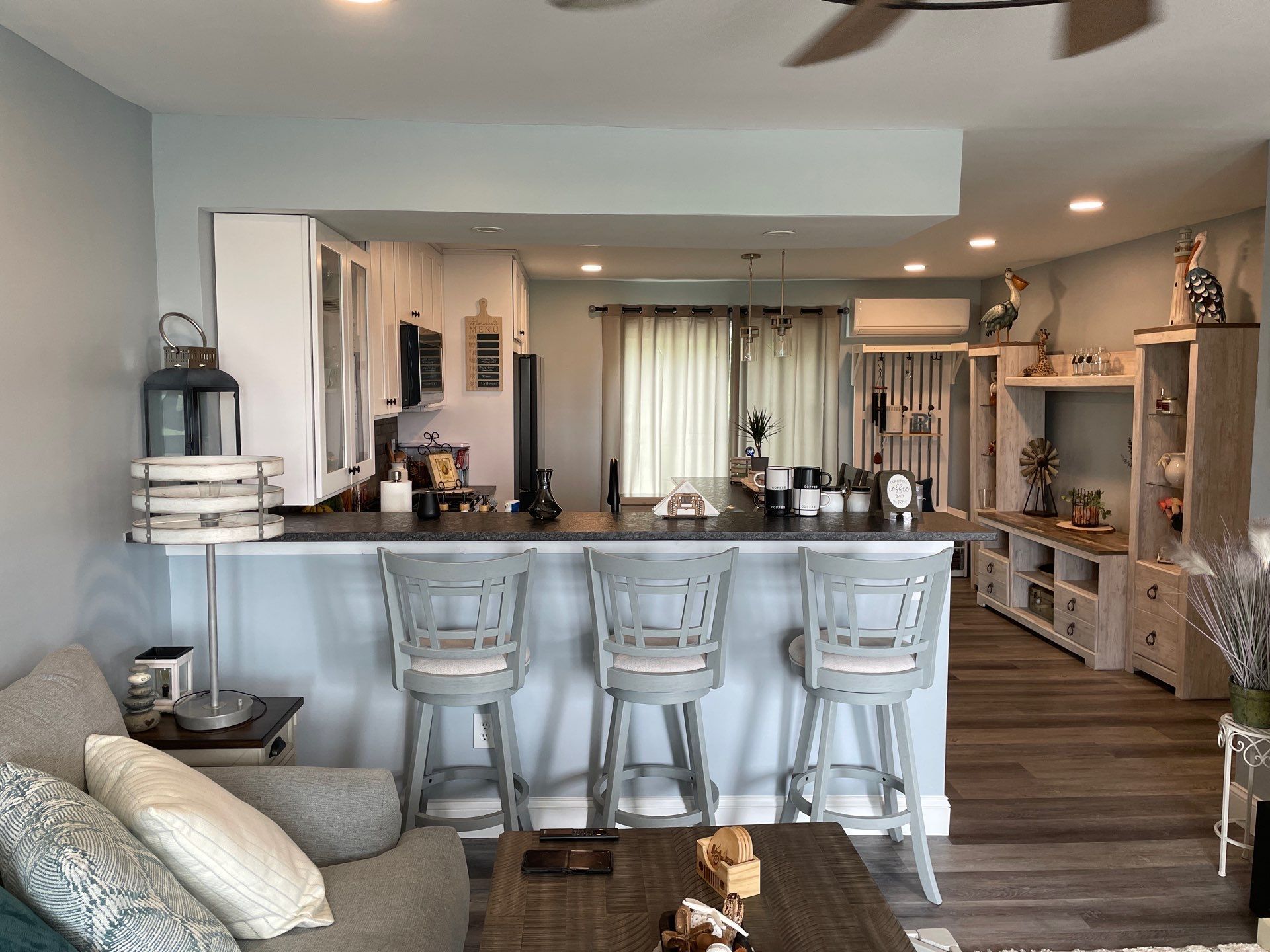 Kitchen with bar stools, open to living area with seating and storage; light blues and wood tones.