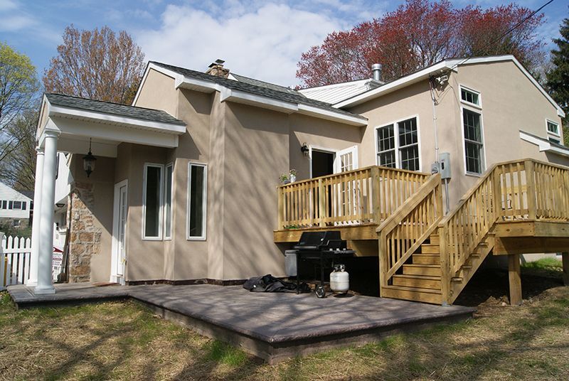 Beige house with wooden deck, patio, and white fence.