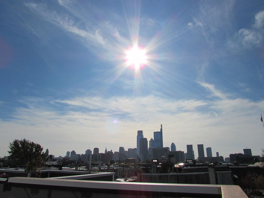 Bright sun over the Philadelphia skyline on a partly cloudy day.